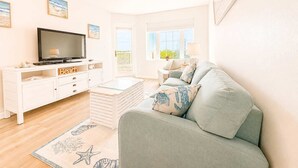 A living room with a television, a ceiling fan, a sofa, a coffee table, and a window with a view. - Grand Caribbean - 315 Newly Remodeled (Orange Beach)