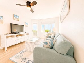 Ein Wohnzimmer mit Fernseher, Deckenventilator, Sofa, Couchtisch und einem Fenster mit Blick.