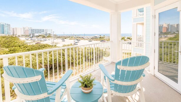 A balcony with two chairs and a small table, overlooking a parking lot and buildings. - Grand Caribbean - 315 Newly Remodeled (Orange Beach)