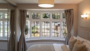 Ein Schlafzimmer mit großem Fenster, einem Bett mit weißer Bettwäsche und einer Wandleuchte.