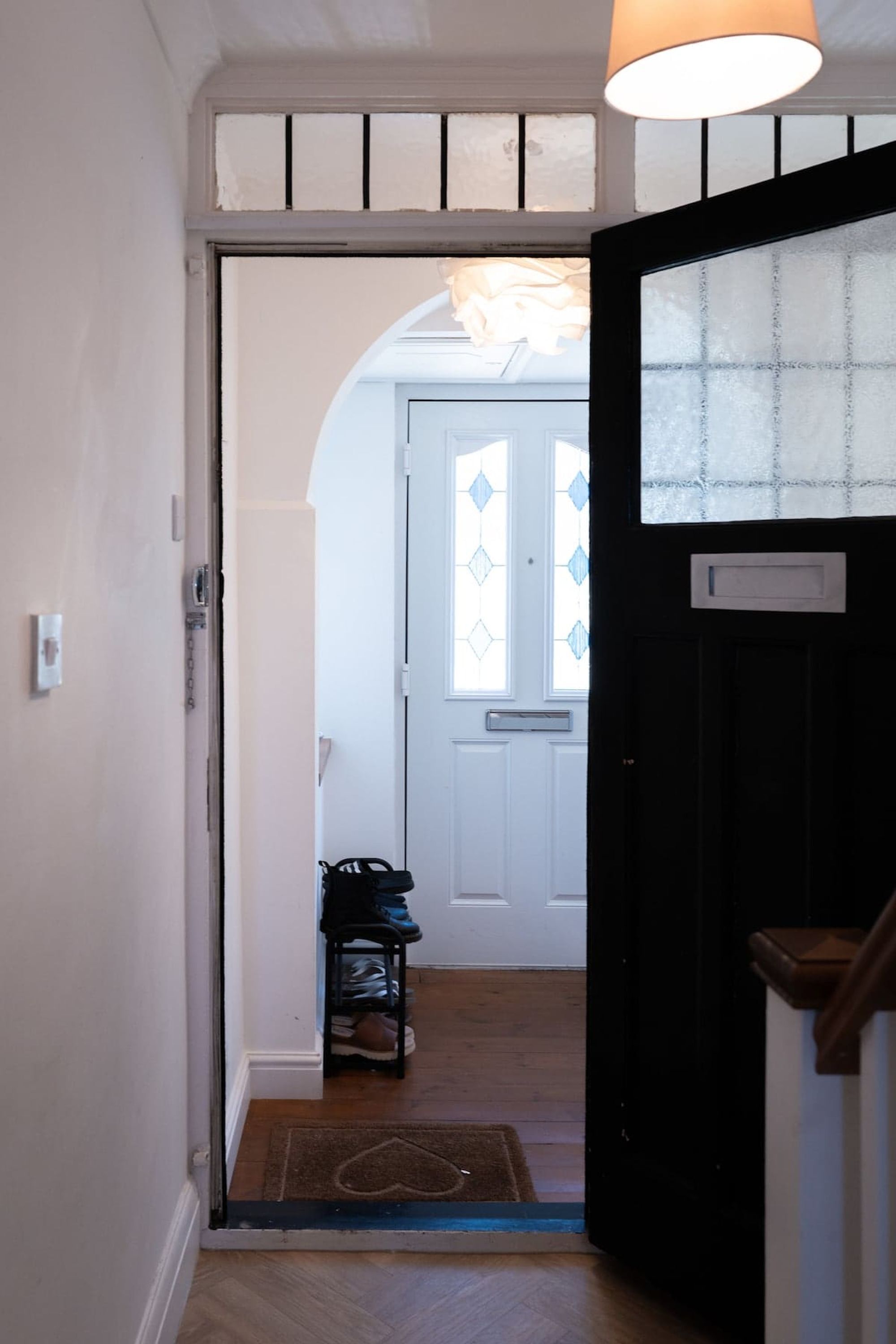 A hallway leading to a door with a doormat and a small stool.