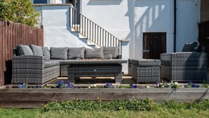 Eine Terrasse mit Korbmöbeln, ein Holzboden und ein weißes Gebäude im Hintergrund.