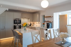 A modern kitchen with white cabinetry, a central island with bar stools, and a dining table with chairs. - Perfect Booking Modern Home By High Street (Rochester)