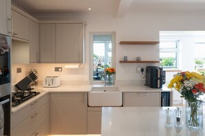 Cozinha moderna com armários brancos, forno embutido, máquina de café e um vaso com flores no balcão.
