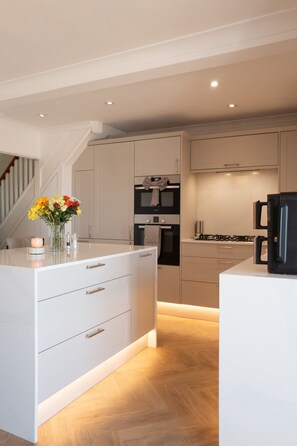 A modern kitchen with white cabinetry, a central island, and a black coffee machine. - Perfect Booking Modern Home By High Street (Rochester)