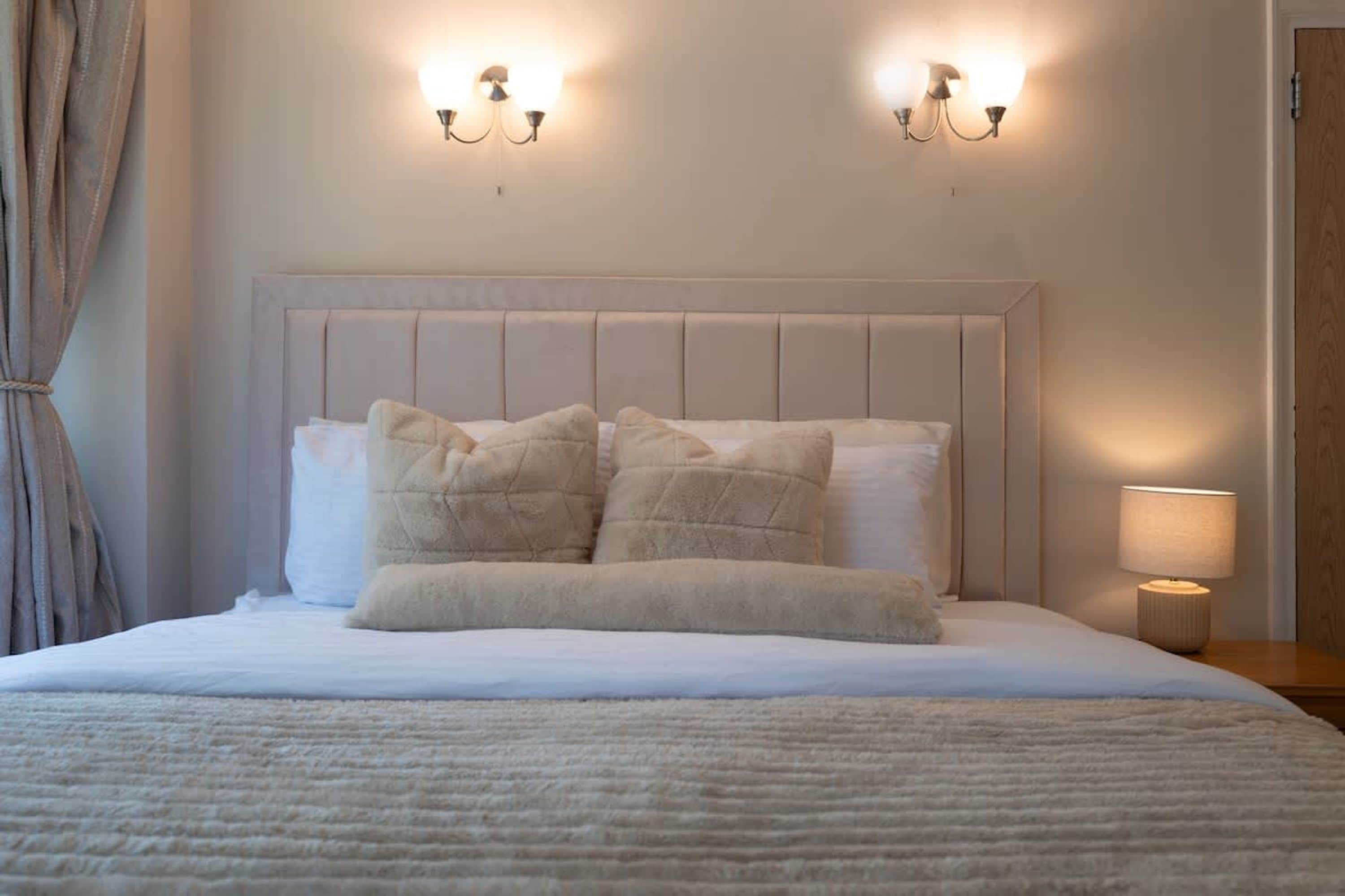 A neatly made bed with a headboard, two wall-mounted light fixtures, and a bedside lamp.