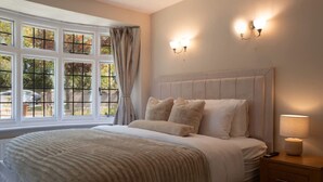 Ein Schlafzimmer mit einem großen Bett, einem Nachttisch mit Lampe und einem Fenster mit Vorhängen.