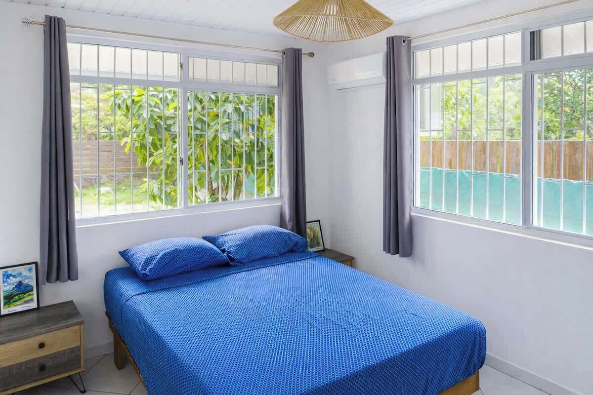 Een slaapkamer met een bed, twee ramen, een nachtkastje en een hanglamp.
