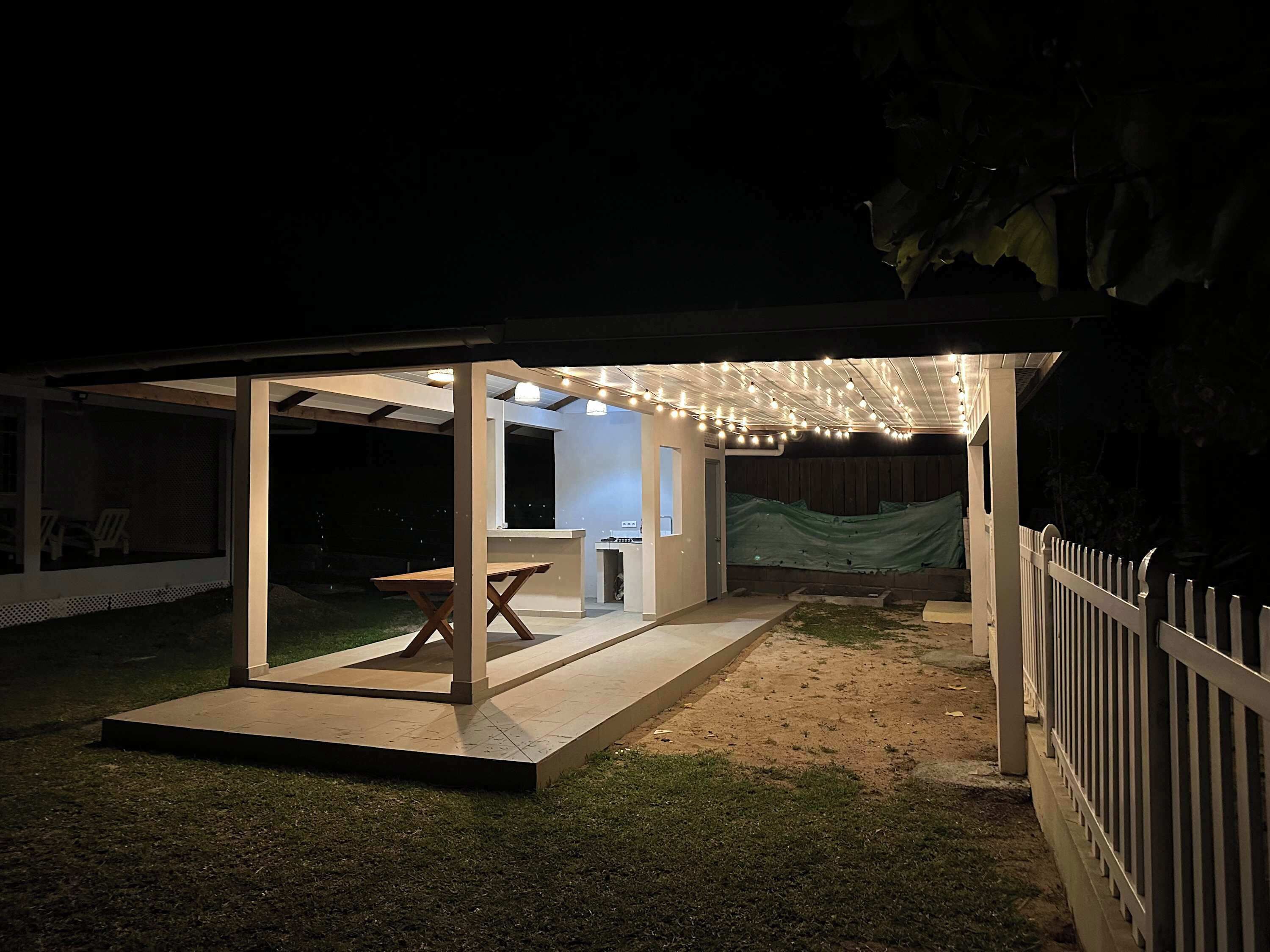 Un patio al aire libre con un área de estar techada, una mesa y un pequeño espacio tipo cocina.