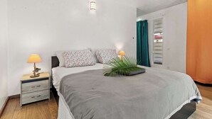 Quarto com cama, luminárias de cabeceira, mesa de apoio, janela com cortinas e porta.