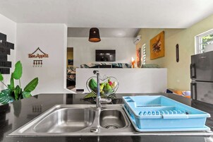 A modern kitchen with a stainless steel sink, a blue dish rack, and a decorative wall hanging.