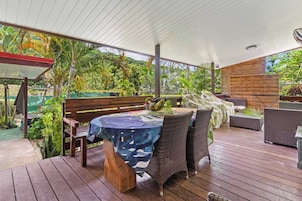 An outdoor patio with wooden flooring, wicker furniture, and a table covered with a blue tablecloth.