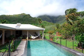 A pool area with a house, a hammock, and a view of a mountainous landscape. - Dolce Vita Villa Moorea (Moorea-Maiao)