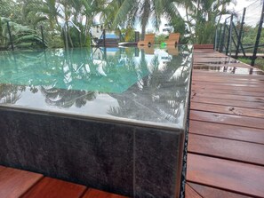 A glass-top pool with a wooden deck, surrounded by palm trees. - Dolce Vita Villa Moorea (Moorea-Maiao)