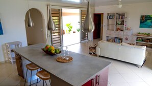 A modern kitchen with a central island, bar stools, and a dining area with a white sofa. - Dolce Vita Villa Moorea (Moorea-Maiao)