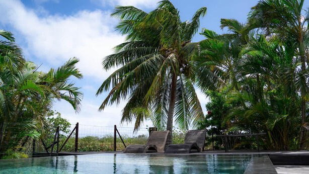 A swimming pool with lounge chairs, surrounded by palm trees. - Dolce Vita Villa Moorea (Moorea-Maiao)