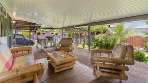 An outdoor covered patio with bamboo furniture, a table, and a car parked nearby. - Peaceful 2BR Garden Bungalow (Taiarapu-Est)