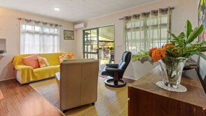 A living room with a sofa, armchair, and a vase with flowers on a table. - Peaceful 2BR Garden Bungalow (Taiarapu-Est)