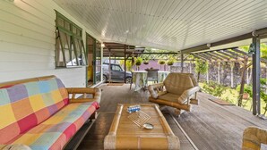 A covered porch with a colorful sofa, a wooden table with a bus model, and a bamboo chair. - Peaceful 2BR Garden Bungalow (Taiarapu-Est)