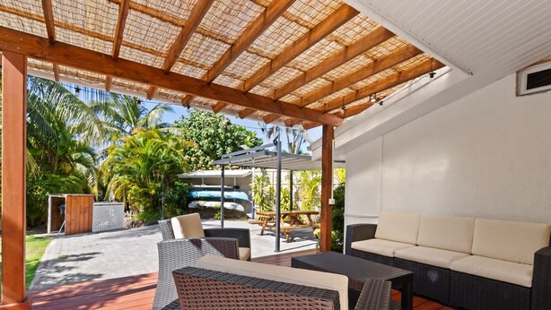 Un patio exterior con mobiliario de mimbre, un sofá blanco y una pérgola con techo de paja.