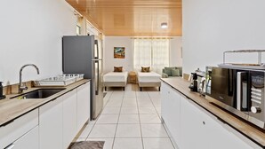 Cocina moderna con refrigerador, microondas y pileta. Hay dos camas con almohadas y un ventanal con cortinas.