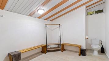 A bathroom with a wooden bench, a hanging shower, and a toilet.