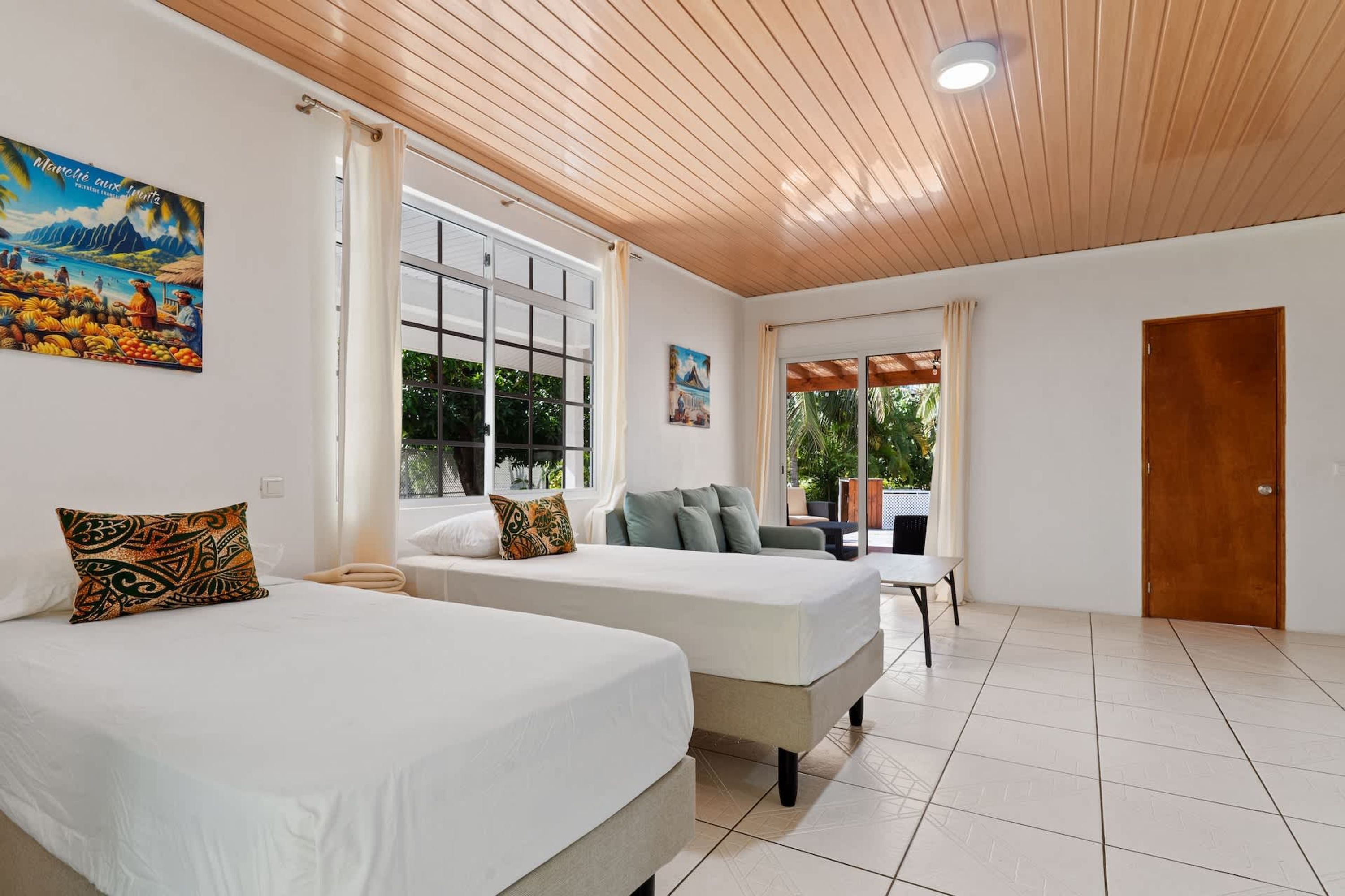 A hotel room with two beds, a wooden ceiling, large windows, and a door.