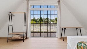 A room with a bed, a small table, a swing, and a view of palm trees through a window. - Moorea Mahana House With Private Canal to Lagoon (Moorea-Maiao)