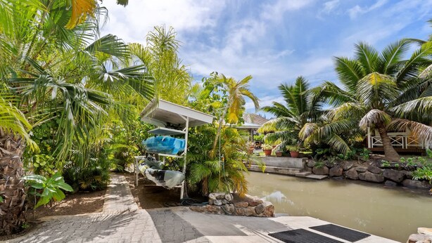 A tropical garden with a paved pathway leading to a water feature, surrounded by lush greenery and palm trees. - Moorea Mahana House With Private Canal to Lagoon (Moorea-Maiao)