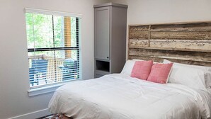 Un dormitorio con cama, un banco, una ventana con persianas y un cabecero de madera.
