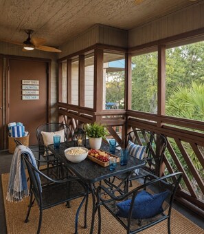 A covered outdoor dining area with a table, chairs, and a view of greenery. - Condo by the beach in Heron Point. (Myrtle Beach)