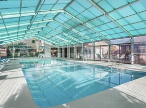 An indoor swimming pool with a glass ceiling, clear water, and lounge chairs. - Condo by the beach in Heron Point. (Myrtle Beach)