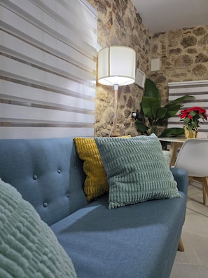 Una sala de estar con un sofá azul, una lámpara, una planta y una pared de piedra.
