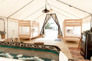 A tent with two bunk beds, a chair, a small table, and a hanging light fixture.