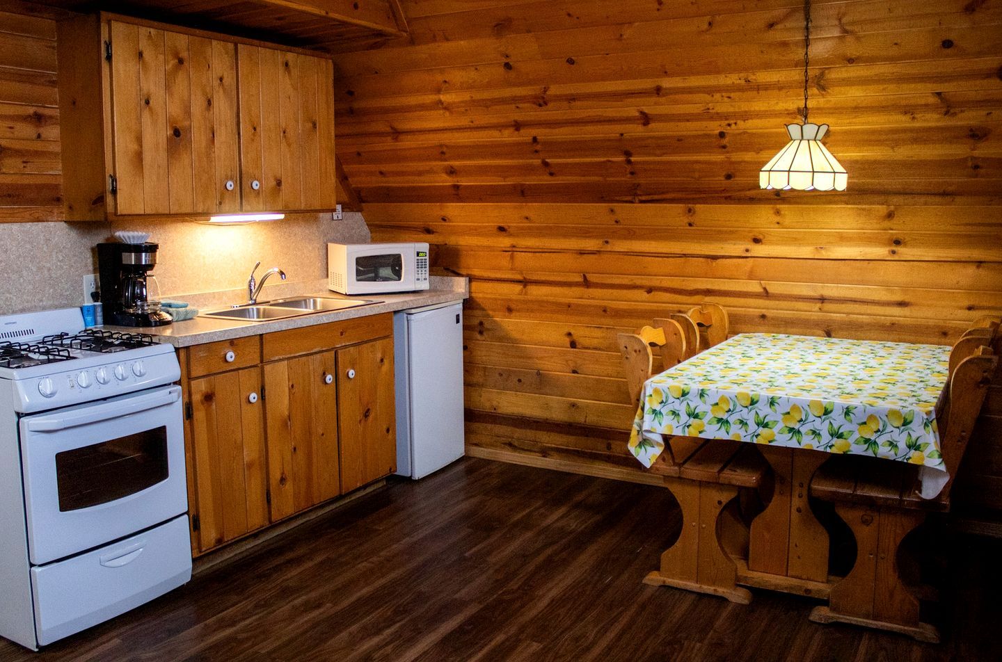Una cocina con armarios de madera, estufa, microondas y una mesa con mantel de limón.