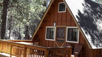 Une cabane dotée d’une terrasse en bois, d’une cheminée et de deux fenêtres.