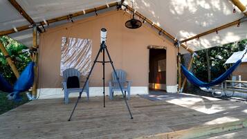 A covered outdoor area with a telescope, two chairs, a hammock, and a wooden deck.