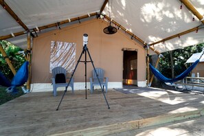 Un espace extérieur abrité comprenant un télescope, deux chaises, un hamac et une terrasse en bois.