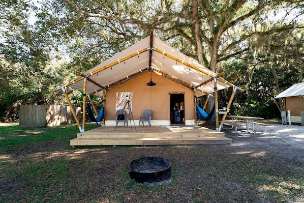 A tent with a porch, two chairs, a hammock, and a grill.