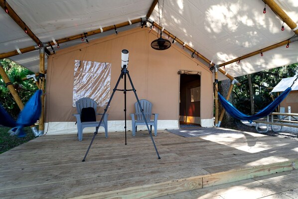 Un espacio al aire libre cubierto con un telescopio, dos sillas, una hamaca y una terraza de madera.