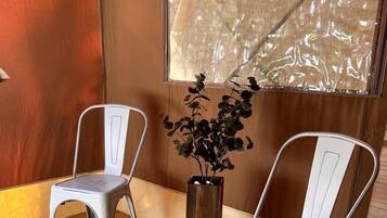 Two white metal chairs, a wooden floor, a window with a view, and a potted plant.