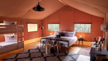 A tent-style room with bunk beds, a central bed, a desk with a chair, and a window with a view.
