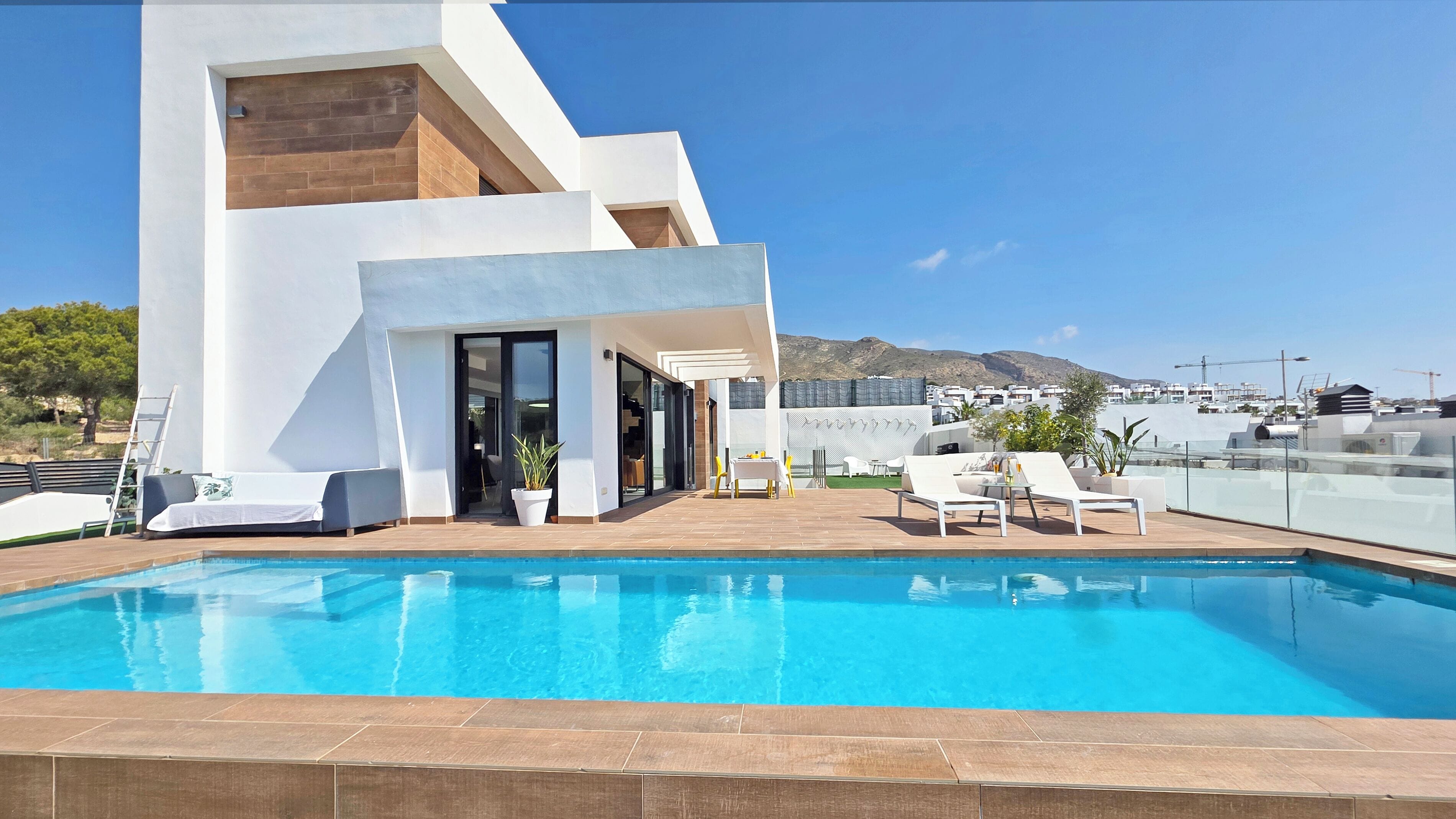 Un espace moderne aménagé au bord de la piscine, offrant une vue dégagée sur la mer et les montagnes en arrière-plan.