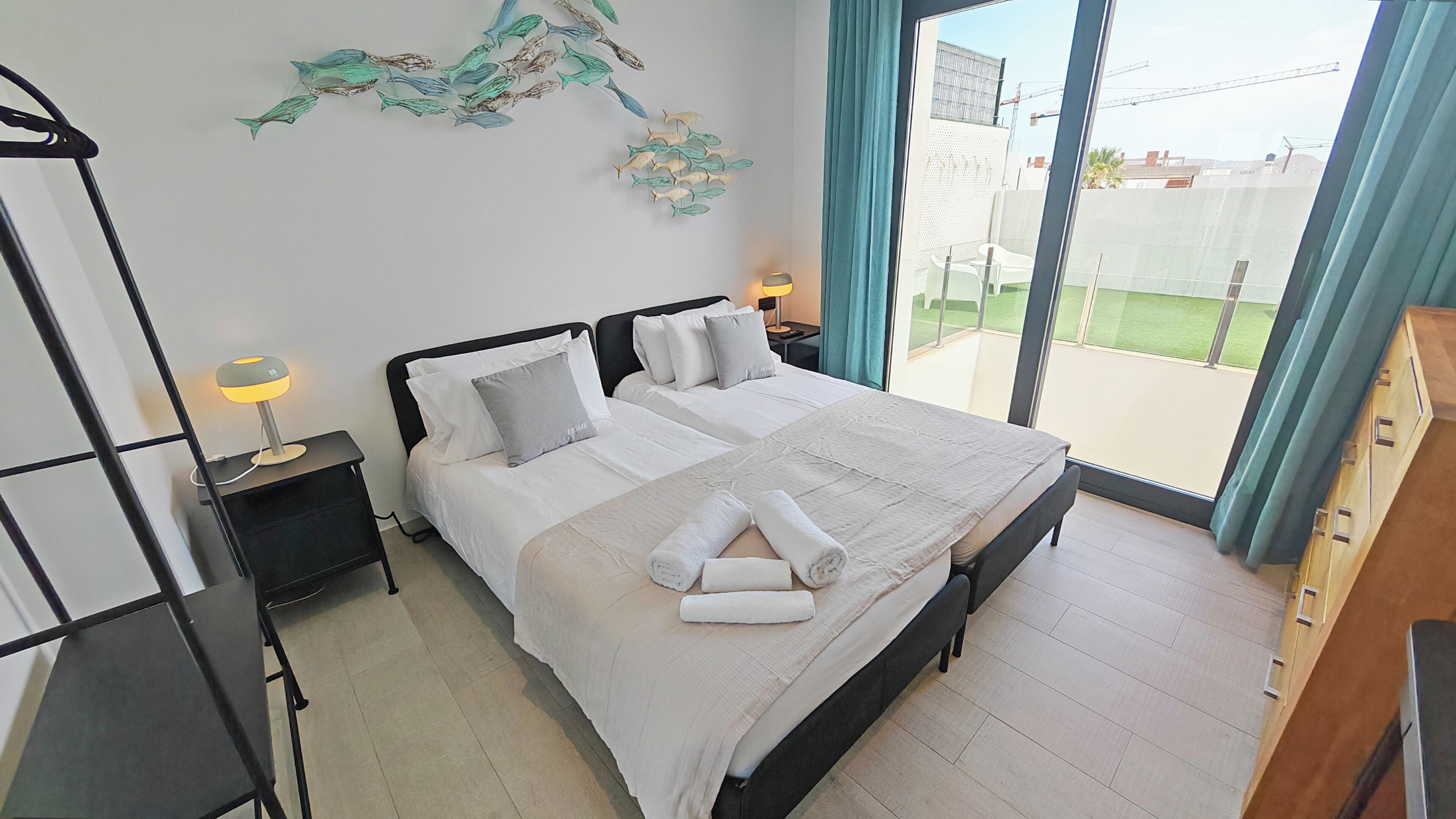A bedroom with a bed, bedside tables, a wall art of fish, and a view of a construction site through the window.