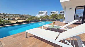 Ein Schwimmbecken mit Liegestühlen und einem Tisch, umgeben von einer gefliesten Terrasse.