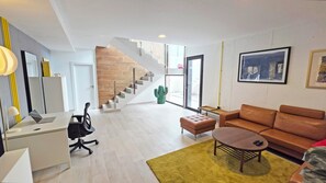 Ein modernes Wohnzimmer mit Treppe, Schreibtisch, einer Couch und einem Kaktus.