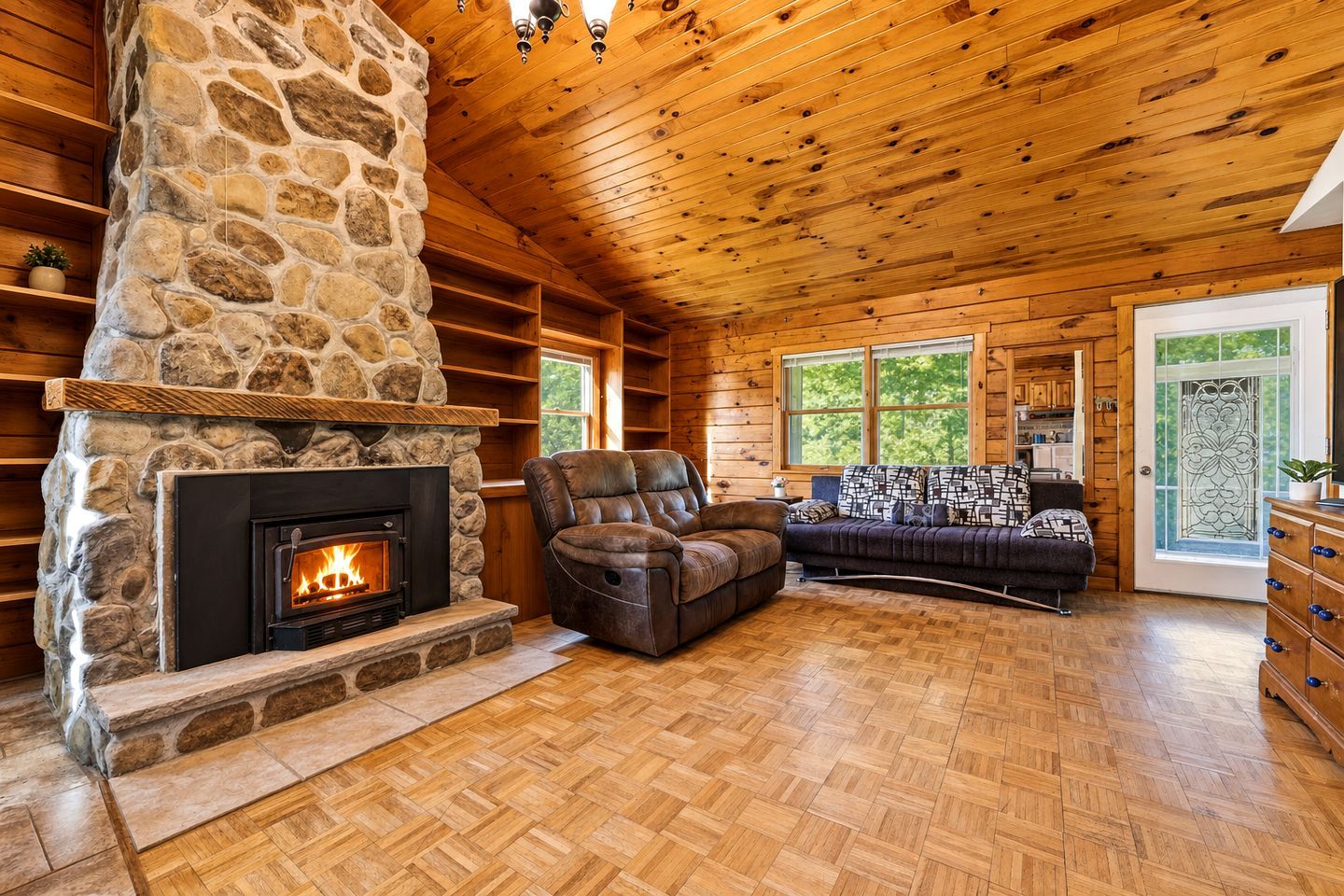 A cozy cabin interior with a stone fireplace, wooden ceiling, and a comfortable seating area.