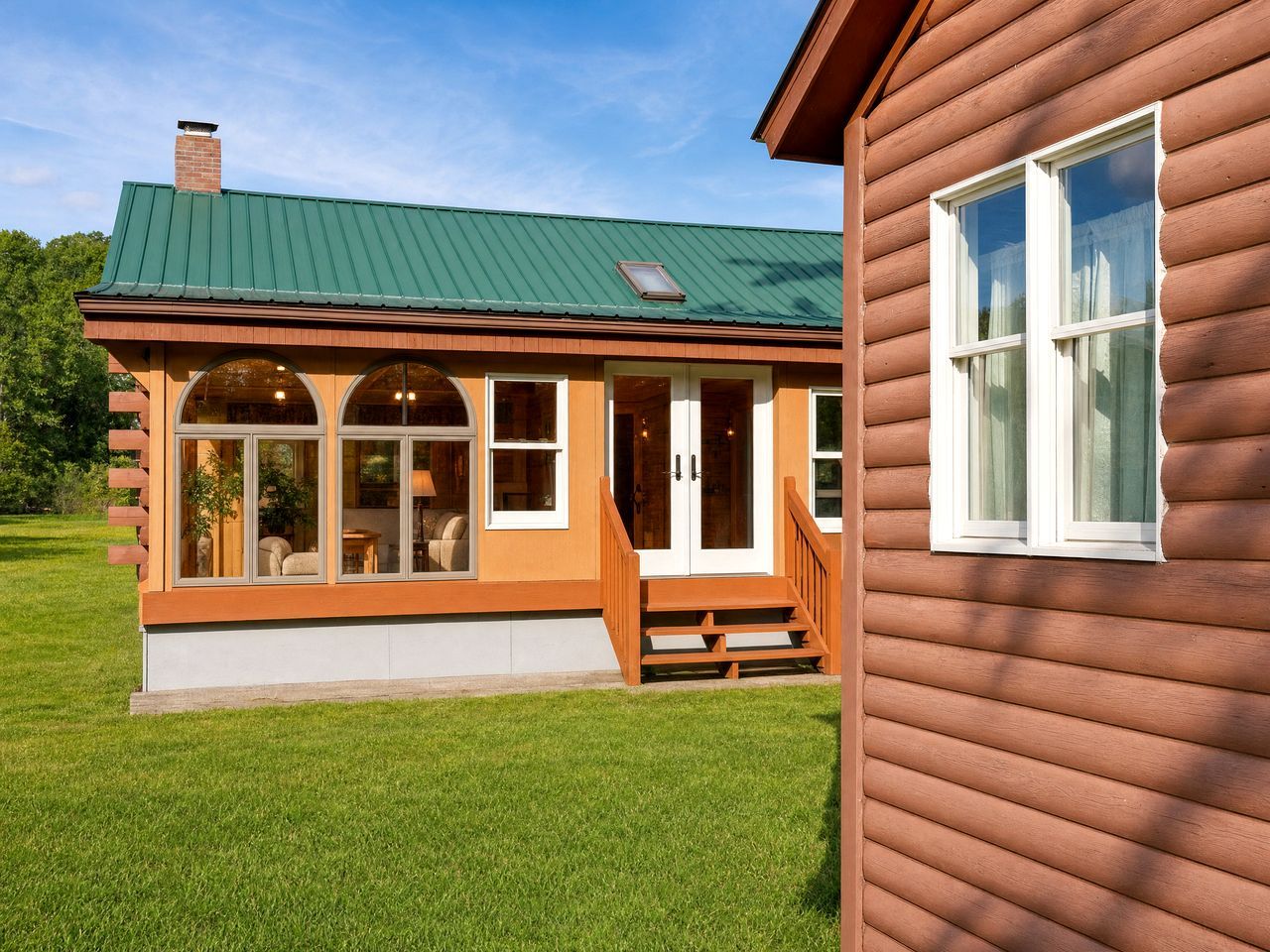 Puurakenteinen talo, jossa on vihreä katto, suuret ikkunat ja kuisti.