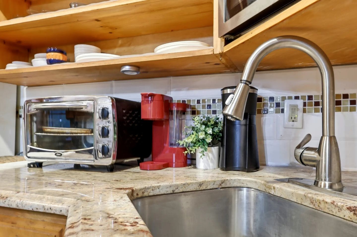 A kitchen with a stainless steel sink, a toaster, a coffee maker, and a potted plant.