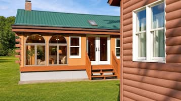 Une maison en bois avec un toit vert, de grandes fenêtres et une véranda.